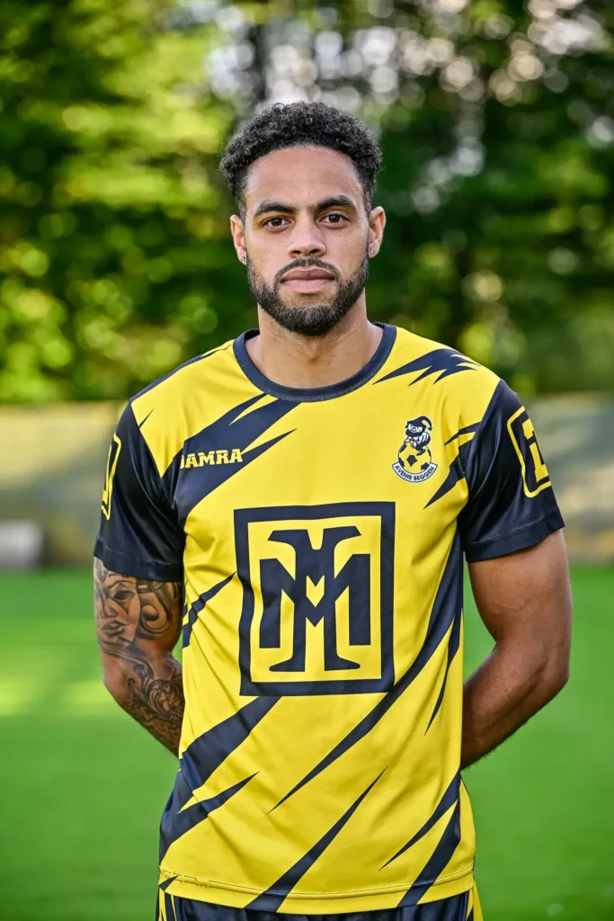 A player from the first team in his kit, posing on the pitch