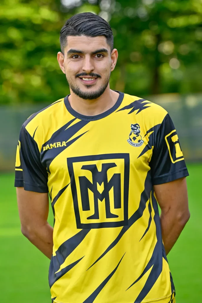 A player from the first team in his kit, posing on the pitch